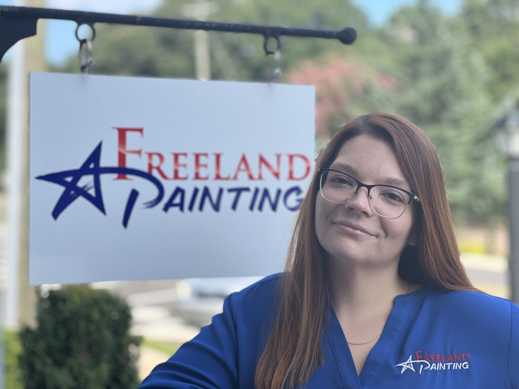 Amanda Fulks, Operations Manager at Freeland Painting in front of Freeland Painting sign.